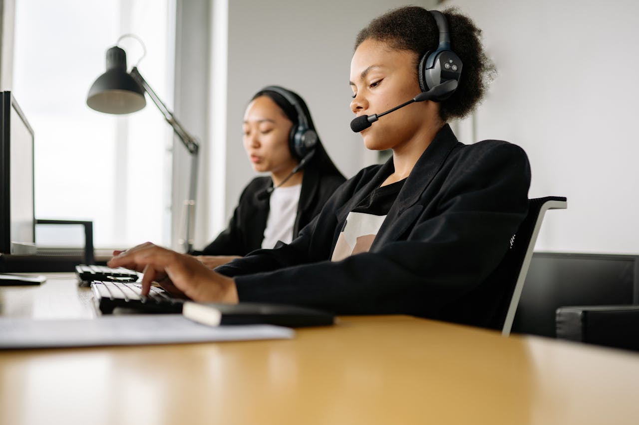 hero-img-02 Two call center agents working at desks in an office setting with headsets.